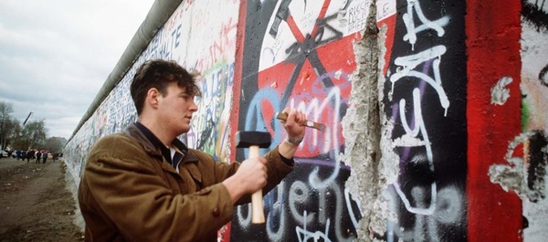 A West German man uses a hammer and chisel to chip off a piece of the Berlin Wall as a souvenir.  A portion of the Wall has already been demolished at Potsdamer Platz; see photo below.