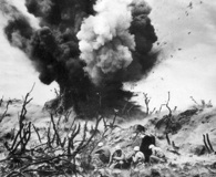 Marines shelter behind a rocky ledge on Iwo Jima as a satchel charge destroys a Japanese pillbox. (National Archives)