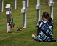 A descendant of a World War II 10th Mountain Division Soldier relaxes at the grave marker of her fallen relative at the Florence American Cemetery in Northern Italy. (Sgt. 1st Class John Queen)