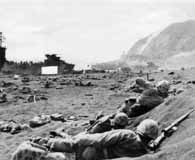 February 1945. Marines take cover in the black volcanic sand of Iwo Jima as they try to advance off the beach. Mount Suribachi can be seen in the background. (National Archives)