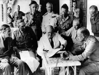 Churchill confers with Allied Leaders in North Africa. (Left to right around the table) Anthony Eden, Gen. Sir Alan Brooke, Air Chief Marshal Sir Arthur Tedder,  Adm. Sir Andrew B. Cunningham, Gen. Sir Harold R.L.G. Alexander, Gen. George C. Marshal, and Gen. Dwight D. Eisenhower. Standing at extreme right is Gen. Sir Bernard Montgomery. National Archives.