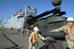 Soldiers unloading aircraft from a massive sea transport ship.